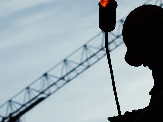 Gázhegesztő sziluettje ipari, magasépítési munkaterületen, daruval a háttérben